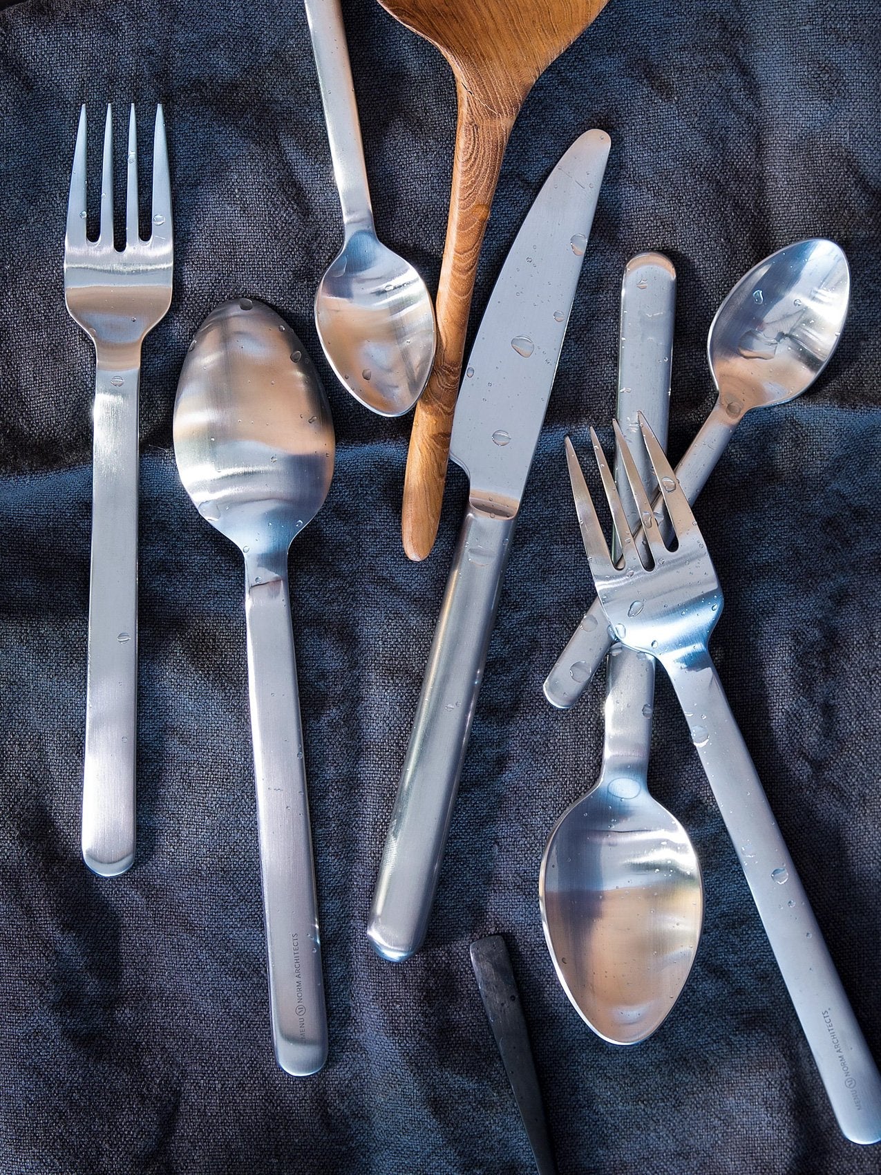 New Norm Flatware by Audo styled on dark linen with a wooden spoon – In Dubai by WSPR