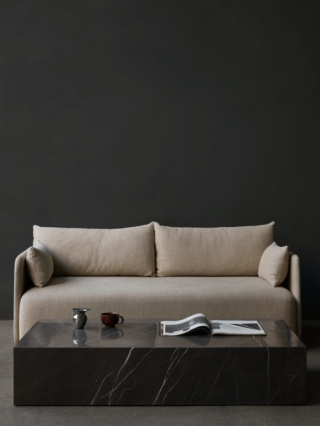 Plinth Table Grand by Audo styled in front of a sofa against a dark wall, with a magazine and small pots – In Dubai by WSPR
