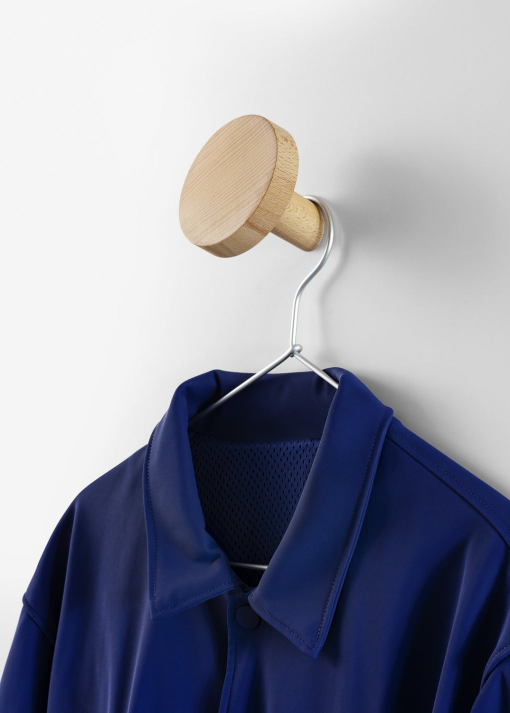 Chiodo Hanger by Miniforms in natural beech, holding a blue jacket on a coat hanger – In Dubai by WSPR