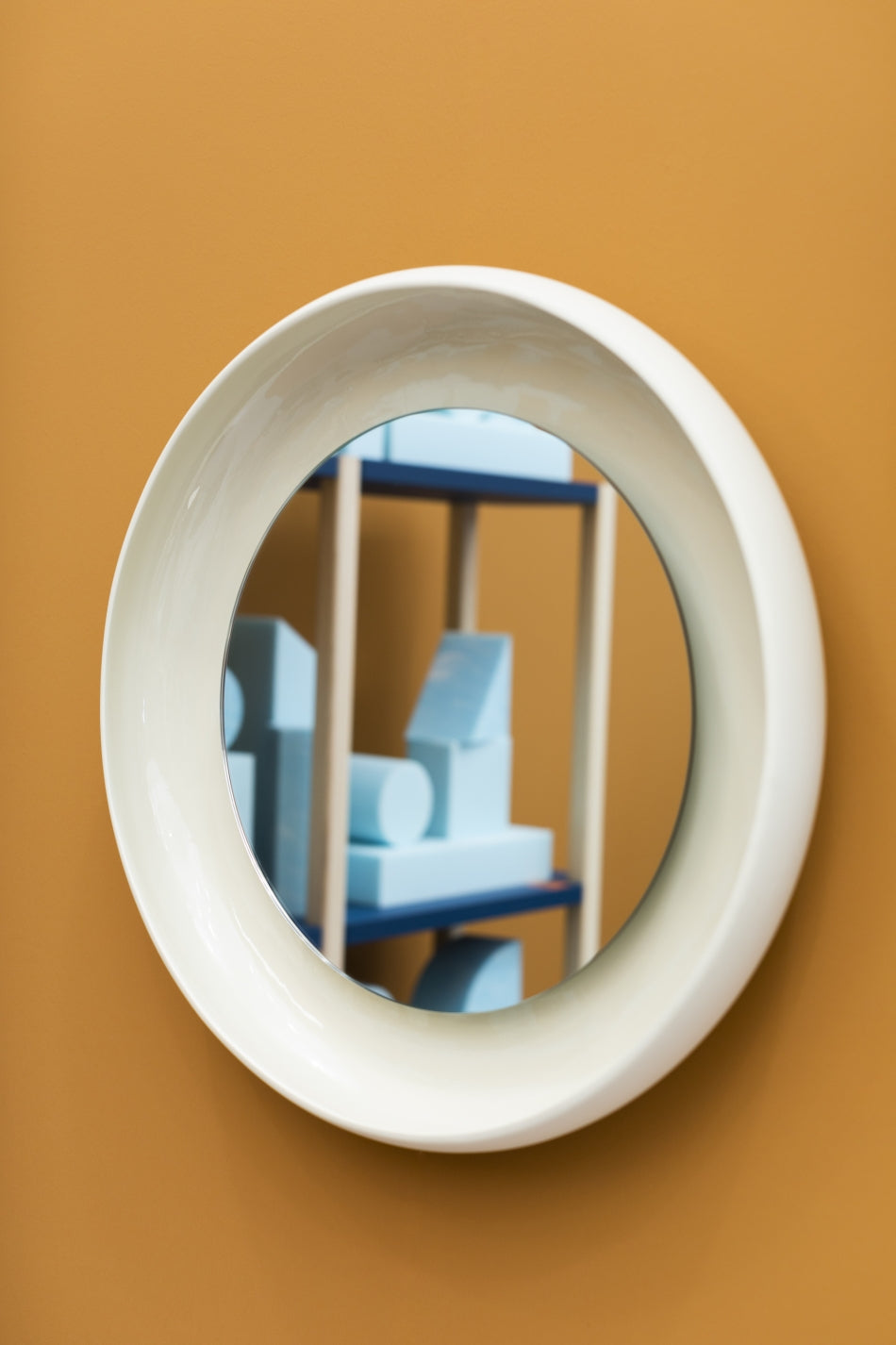 Coque Mirror by Miniforms in cream glazed ceramic, reflecting a shelf, on an ochre wall – In Dubai by WSPR