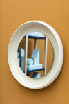 Coque Mirror by Miniforms in cream glazed ceramic, reflecting a shelf, on an ochre wall – In Dubai by WSPR