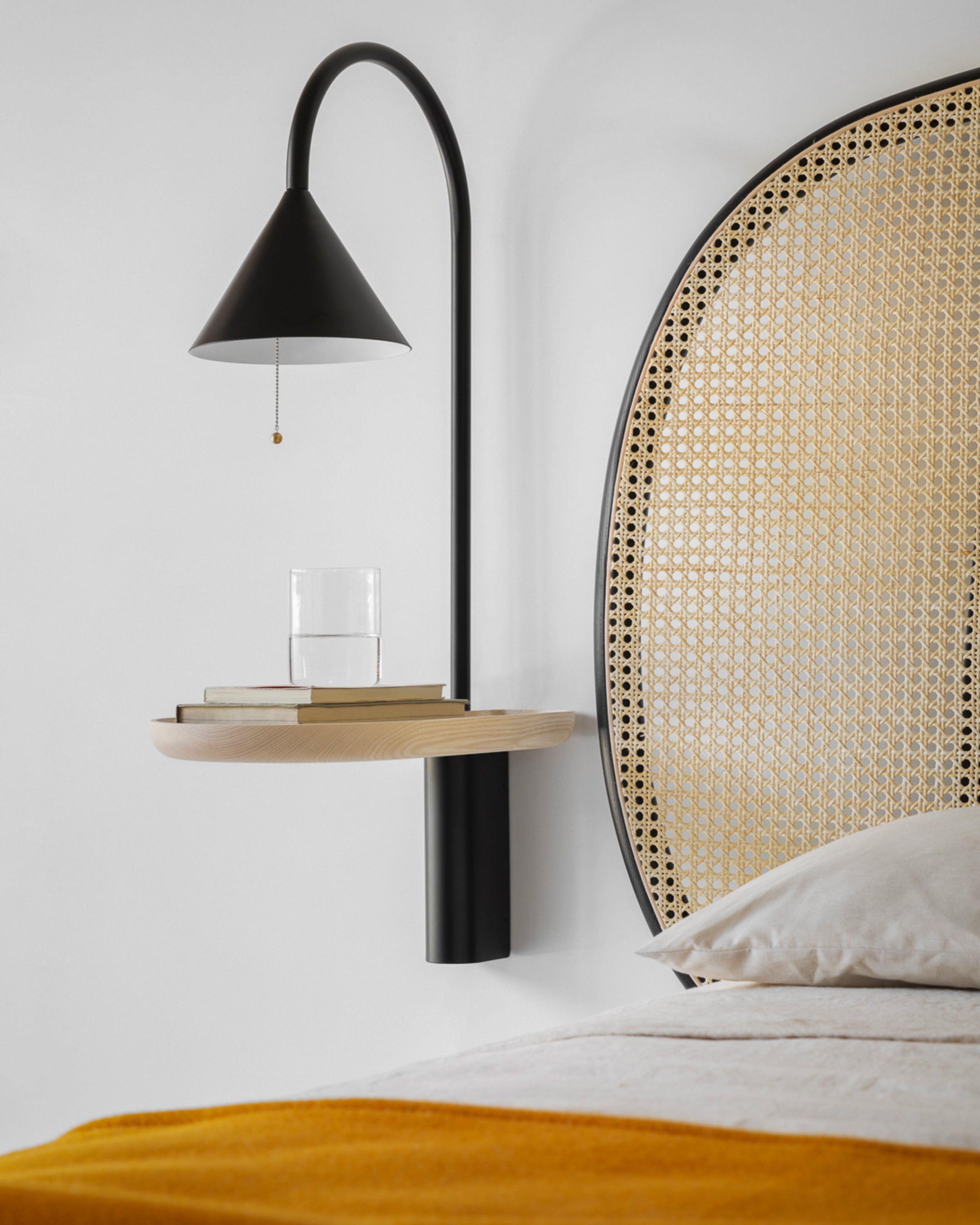 Ozz Wall S Lamp by Miniforms in black metal with an ash shelf, as a bedside light beside a cane headboard – In Dubai by WSPR